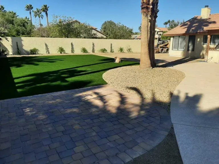 Curved paver patio beside artificial turf and a rock-ring palm tree in Las Vegas