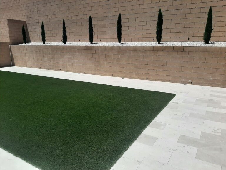 Fresh artificial turf lawn bordered by travertine in a walled Las Vegas backyard by FreshStart Landscaping